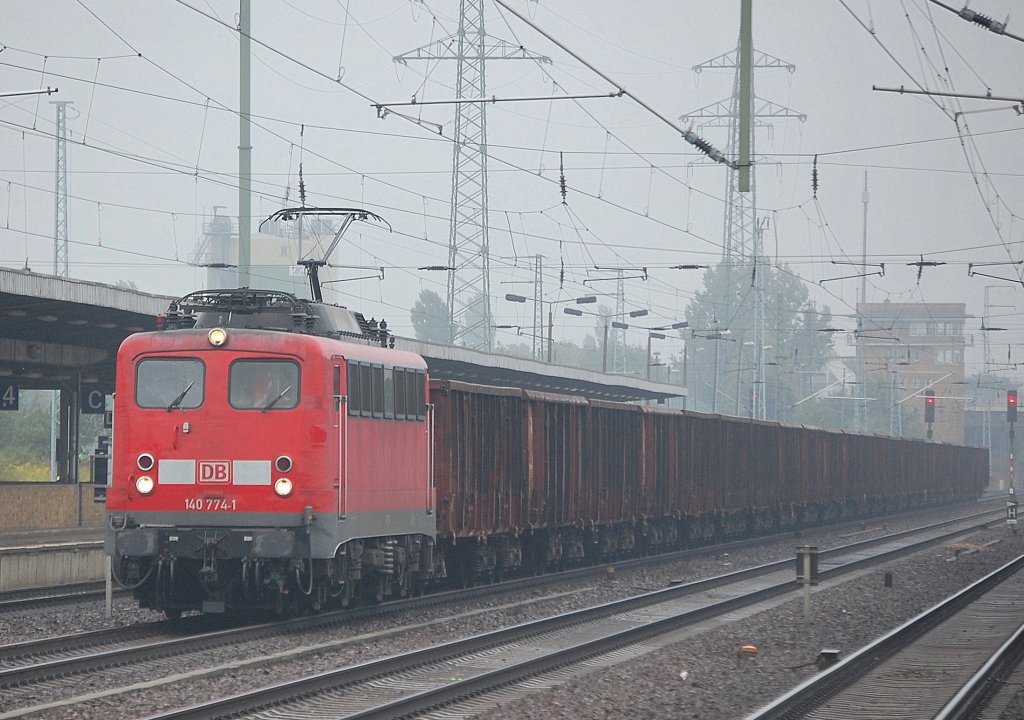 Bei Dauerspr�hregen unterwegs, 140 774-1 mit Ganzzug offener G�terwagen, 09.09.10 Durchfahrt Bhf. Flughafen Berlin-Sch�nefeld. 