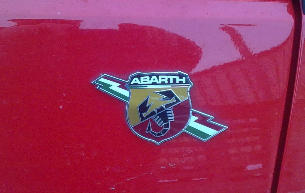 Zwar ist die L�nderkennung sofort erkennbar aber einen Scorpion als Fahrzeuglogo sieht man nun wirklich nicht alle Tage, namentlich ist ABARTH dar�ber zu lesen, es ist die italienische Fahrezeugmarke eines Herstellers von Sportfahrzeugen und selbst produzierten Fahrezeugen in der Vergangenheit und in der Gegenwart von aufgetunten Fiat-Fahrzeugen, gegr�ndet 1949 und seit 1971 bereits zur Fiat Group geh�rend, hier das Seitenlogo eines Abarth Grande Punto, 22.02.13 Berlin-Pankow.
