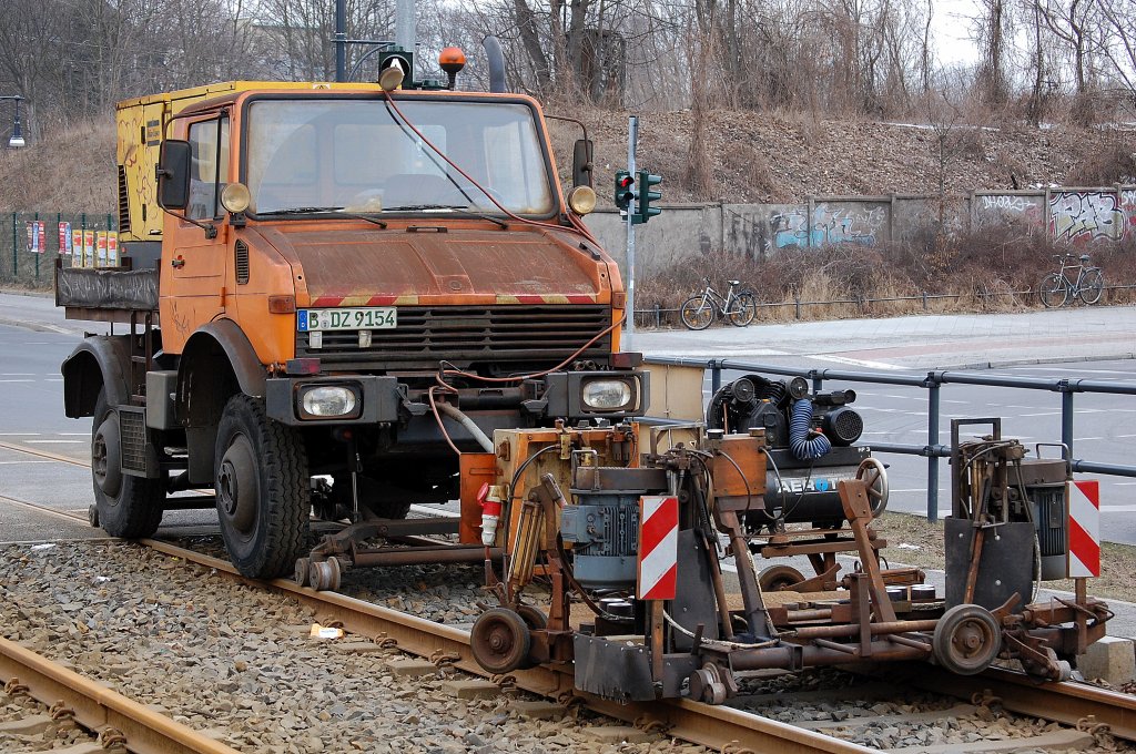 Zweiwege MB Unimog Typ? schiebt und treibt eine Schienenschleifmaschine �ber ein durch Bauarbeiten l�nger nicht genutztes TRAM-Gleis in Berlin, 04.04.13
