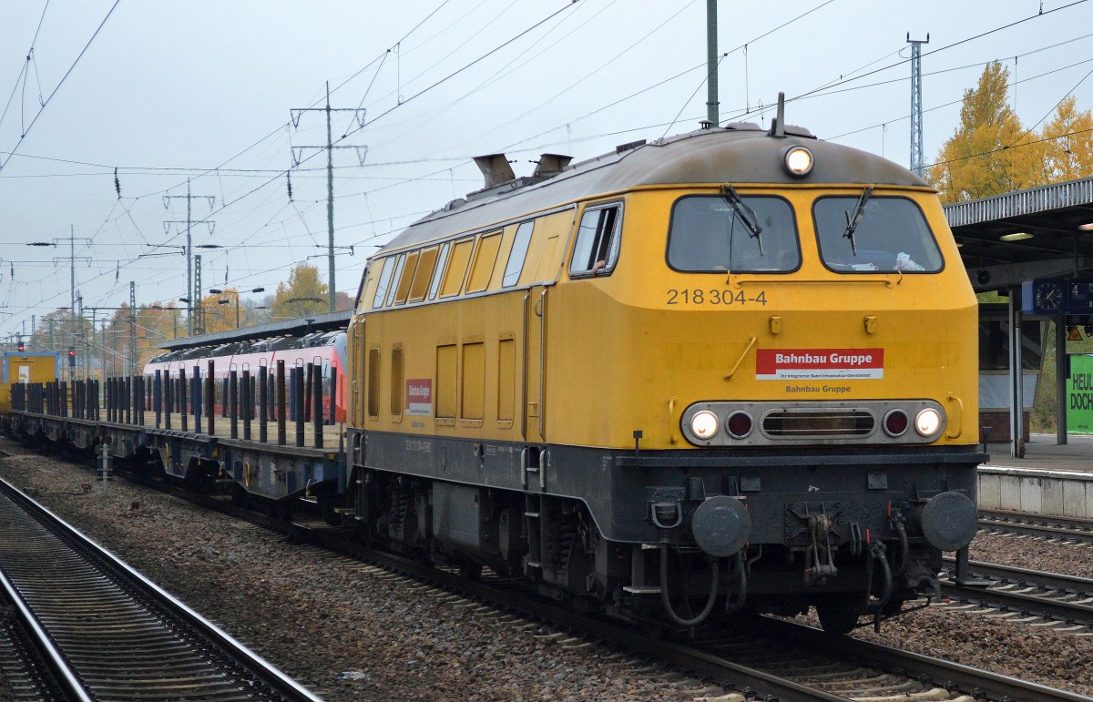 Die Bahnbau Gruppe mit 218 304-4 und einer Reihe leerer Drehgestell-Flachwagen + MATISA Weichentransportwagen (leer) bei der Durchfahrt Bhf. Flughafen Berlin-Schönefeld, 19.10.15