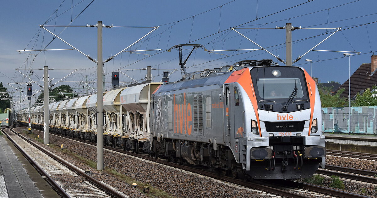 Havelländische Eisenbahn AG, Berlin-Spandau [D] mit ihrer Eurodual Lok  159 010  [NVR-Nummer: 90 80 2159 010-8 D-HVLE] und einem Baustoff-Schüttgutwagenzug (leer) am 22.07.25 Höhe Bahnhof Luckenwalde.